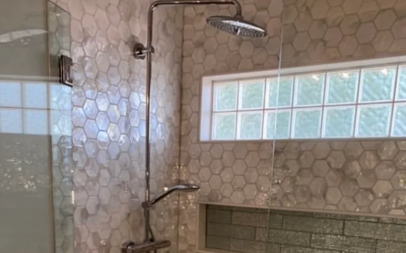 A finished walk-in shower in a remodelled bathroom, hexagonal tile walls with a rainfall head, thermostatic valve and a tiled recessed niche.